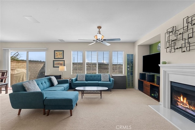 carpeted living room with a ceiling fan and a glass covered fireplace