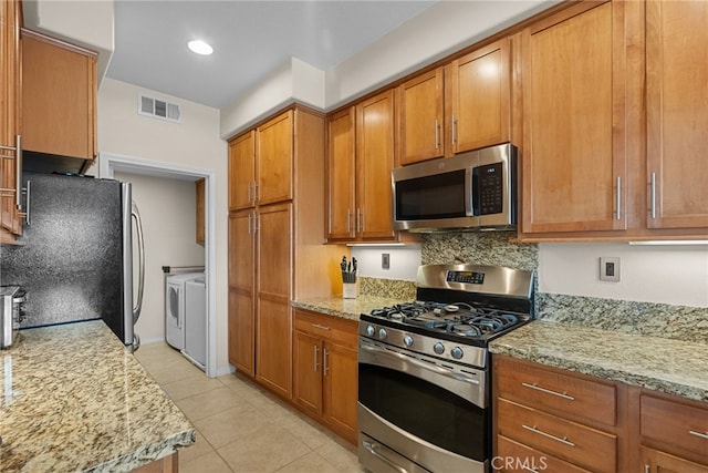 kitchen with visible vents, appliances with stainless steel finishes, brown cabinetry, separate washer and dryer, and light stone countertops