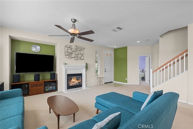 carpeted living area with stairs, a glass covered fireplace, visible vents, and baseboards