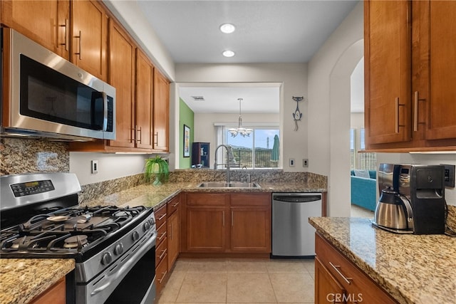 kitchen with stainless steel appliances, brown cabinets, a sink, and light stone counters