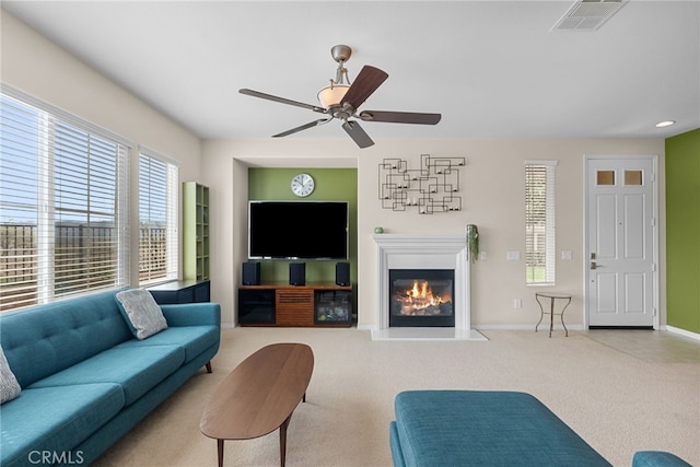 carpeted living room featuring ceiling fan, a glass covered fireplace, visible vents, and baseboards