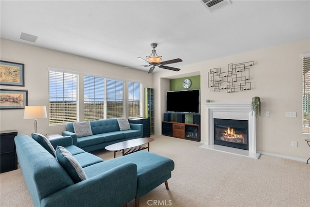 carpeted living room with baseboards, visible vents, a ceiling fan, and a glass covered fireplace