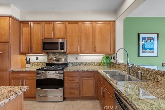 kitchen with stainless steel appliances, brown cabinets, a sink, and light stone counters