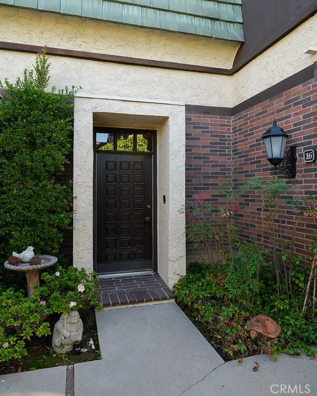 doorway to property featuring stucco siding, mansard roof, and brick siding