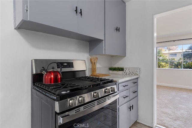 kitchen with stainless steel gas range, light countertops, light carpet, and baseboards