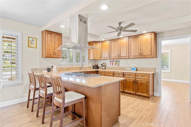 kitchen with light wood finished floors, a breakfast bar area, island exhaust hood, and stainless steel gas stovetop