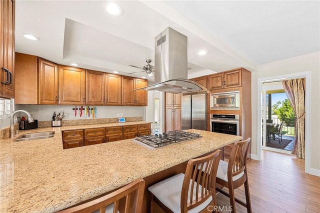 kitchen featuring island range hood, brown cabinets, a sink, and built in appliances