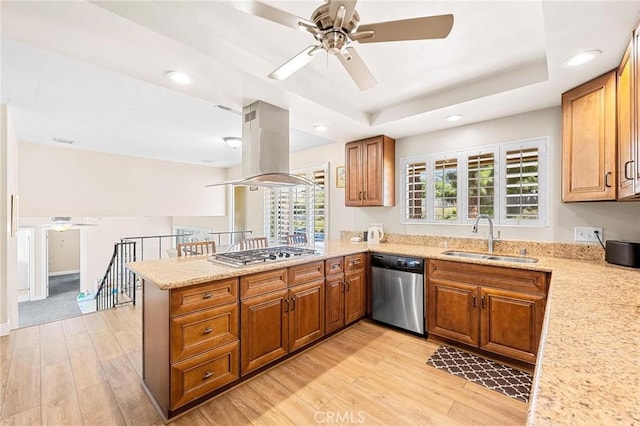 kitchen featuring stainless steel appliances, a sink, light wood-style floors, a tray ceiling, and island exhaust hood