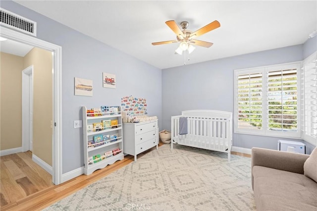 bedroom featuring light wood finished floors, baseboards, visible vents, ceiling fan, and a nursery area