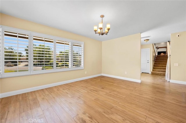 empty room featuring light wood-style flooring, stairs, baseboards, and a notable chandelier