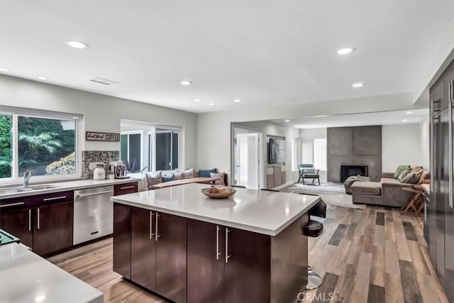 kitchen featuring a sink, light countertops, stainless steel dishwasher, and a tile fireplace