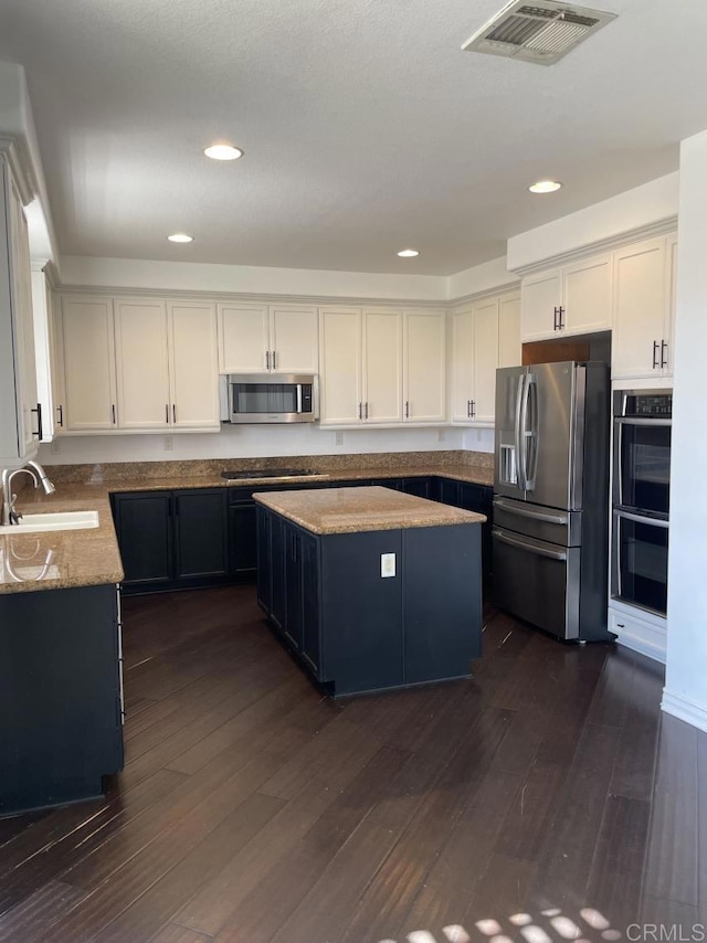 kitchen with stainless steel appliances, a kitchen island, a sink, visible vents, and dark wood finished floors