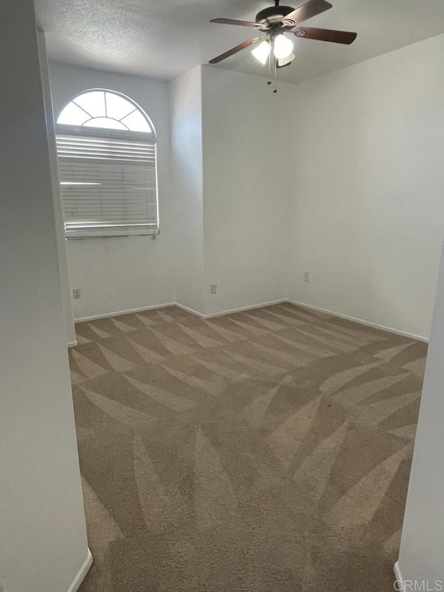 carpeted spare room featuring a textured ceiling, a ceiling fan, and baseboards