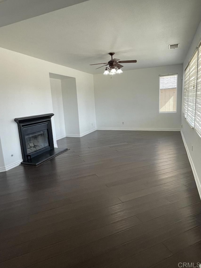 unfurnished living room with a glass covered fireplace, visible vents, dark wood finished floors, and baseboards