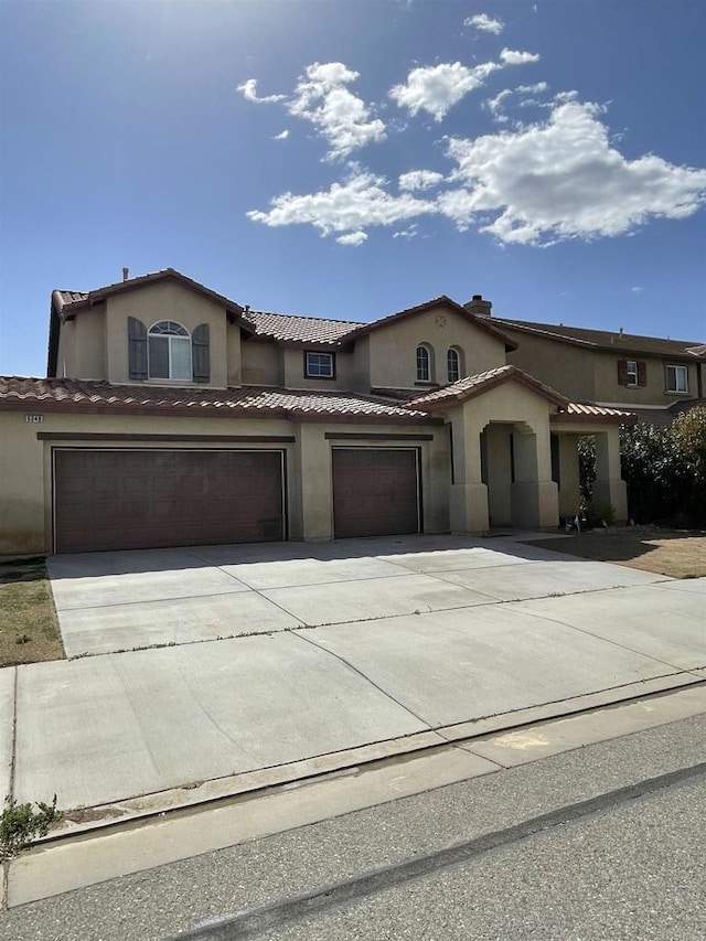 mediterranean / spanish house featuring driveway, a tiled roof, an attached garage, and stucco siding