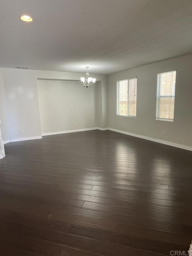 empty room with baseboards, dark wood-style flooring, visible vents, and an inviting chandelier