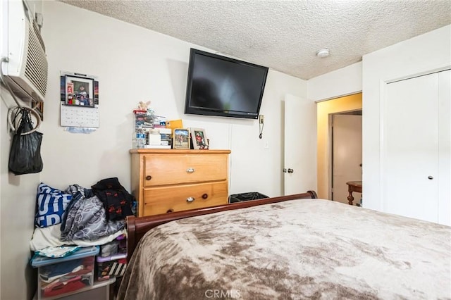 bedroom with a closet, a textured ceiling, and a wall mounted AC