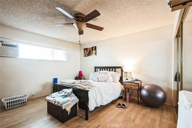 bedroom with a textured ceiling, a wall unit AC, wood finished floors, a ceiling fan, and baseboards