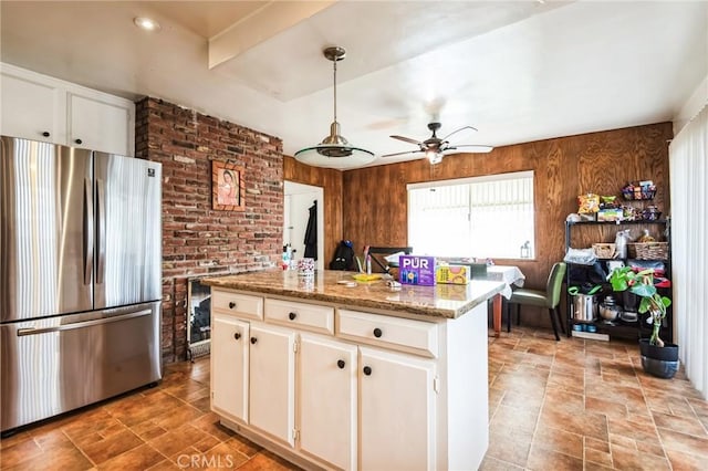 kitchen featuring a center island, freestanding refrigerator, white cabinets, wood walls, and ceiling fan