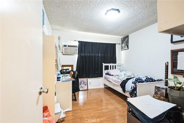 bedroom with a textured ceiling, an AC wall unit, and wood finished floors