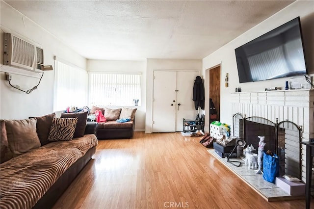 living area featuring an AC wall unit, a fireplace, a textured ceiling, and wood finished floors