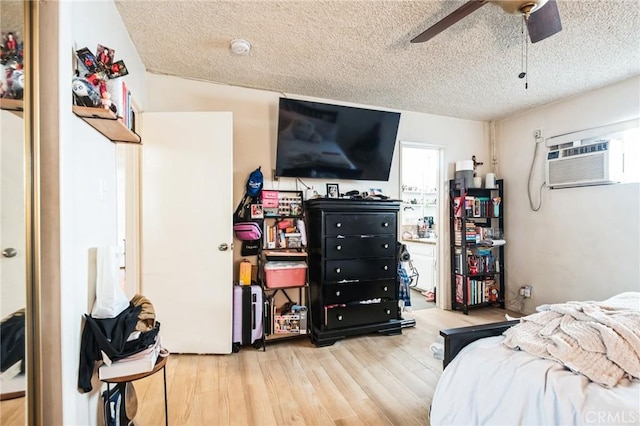 bedroom with a ceiling fan, a wall unit AC, a textured ceiling, and wood finished floors