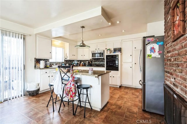 kitchen featuring pendant lighting, backsplash, appliances with stainless steel finishes, white cabinetry, and a kitchen bar