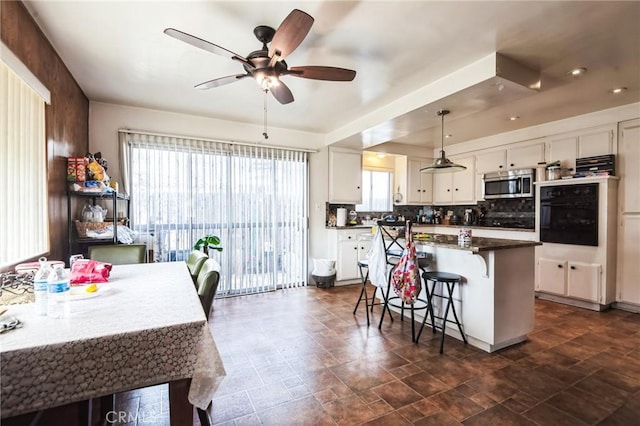 kitchen featuring a breakfast bar area, oven, white cabinetry, tasteful backsplash, and stainless steel microwave