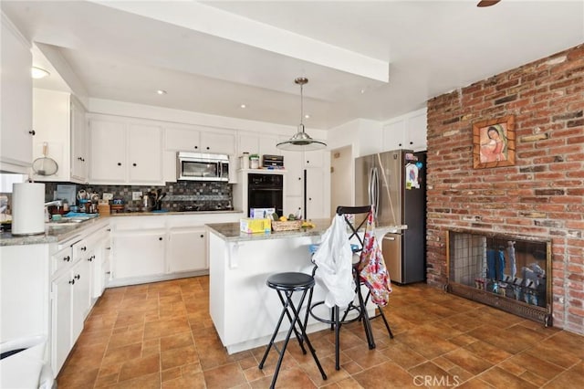 kitchen with appliances with stainless steel finishes, white cabinets, a kitchen island, and backsplash