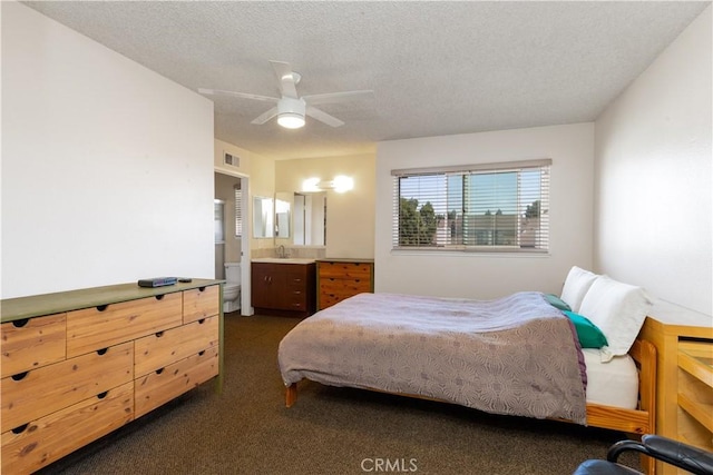 bedroom featuring a textured ceiling, ceiling fan, connected bathroom, visible vents, and dark carpet