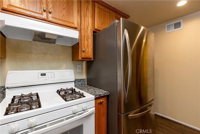 kitchen featuring white gas stove, under cabinet range hood, visible vents, freestanding refrigerator, and brown cabinets