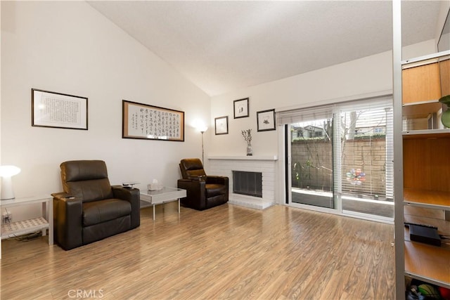 living area with vaulted ceiling, a brick fireplace, and wood finished floors