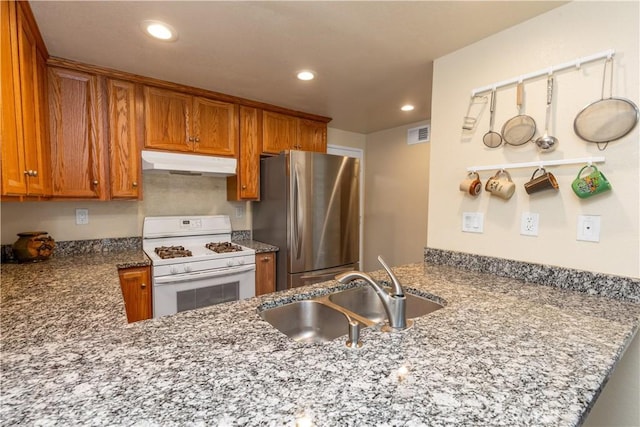 kitchen with freestanding refrigerator, a peninsula, gas range gas stove, under cabinet range hood, and a sink