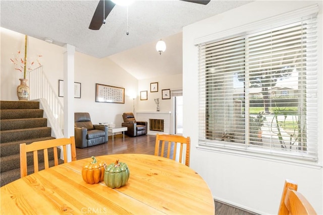 dining area featuring lofted ceiling, a fireplace, wood finished floors, a ceiling fan, and stairway