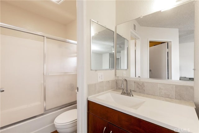 bathroom with visible vents, toilet, enclosed tub / shower combo, vanity, and backsplash