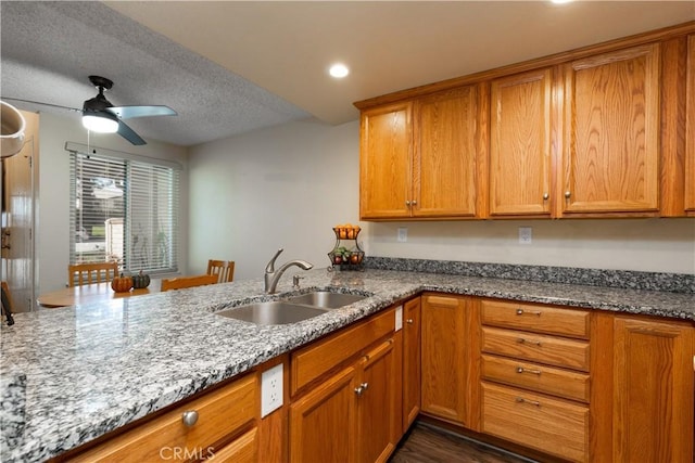 kitchen with brown cabinetry, stone countertops, and a sink