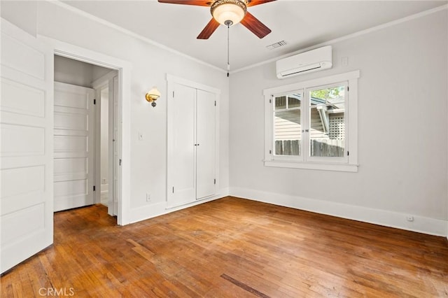 unfurnished bedroom with visible vents, crown molding, baseboards, a wall mounted air conditioner, and hardwood / wood-style floors