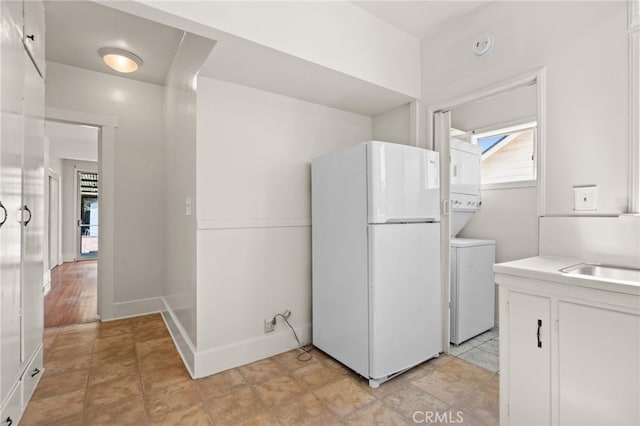 washroom featuring a sink, baseboards, stacked washer and clothes dryer, and laundry area