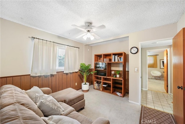 tiled living room with carpet floors, a ceiling fan, a textured ceiling, and wainscoting