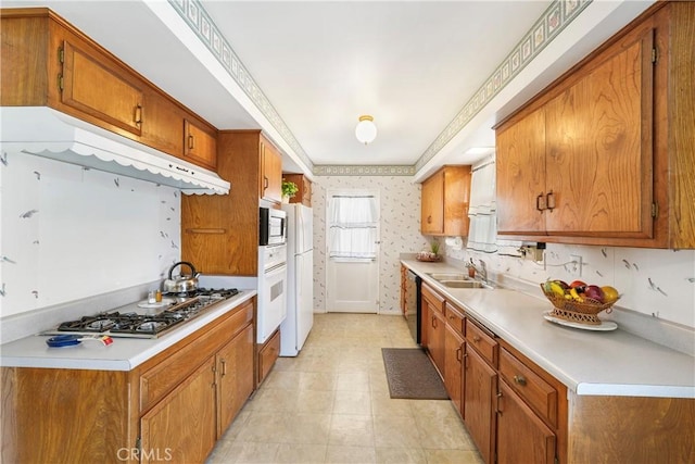 kitchen with under cabinet range hood, a sink, appliances with stainless steel finishes, brown cabinetry, and wallpapered walls