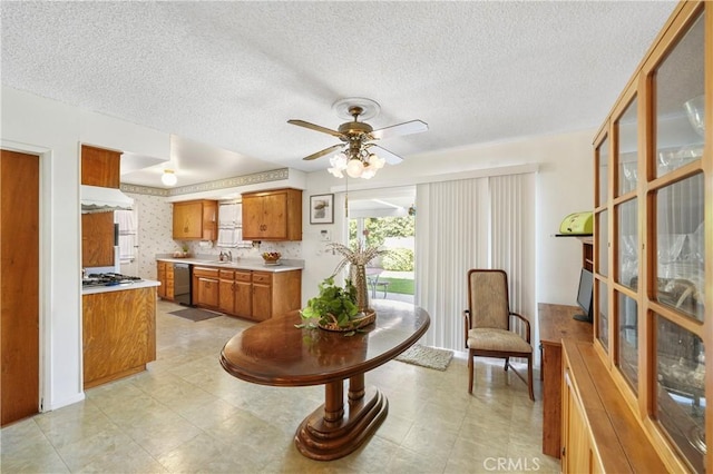 kitchen featuring dishwashing machine, under cabinet range hood, light countertops, brown cabinetry, and wallpapered walls