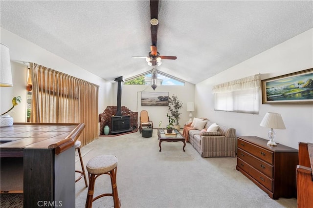 carpeted living room featuring vaulted ceiling with beams, a textured ceiling, a wood stove, and a ceiling fan