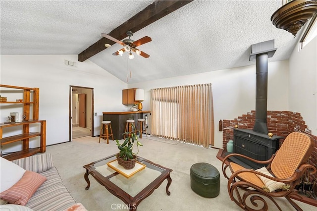 living area featuring a wood stove, visible vents, vaulted ceiling with beams, and carpet flooring