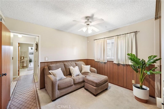 living area with light carpet, wainscoting, ceiling fan, a textured ceiling, and wood walls