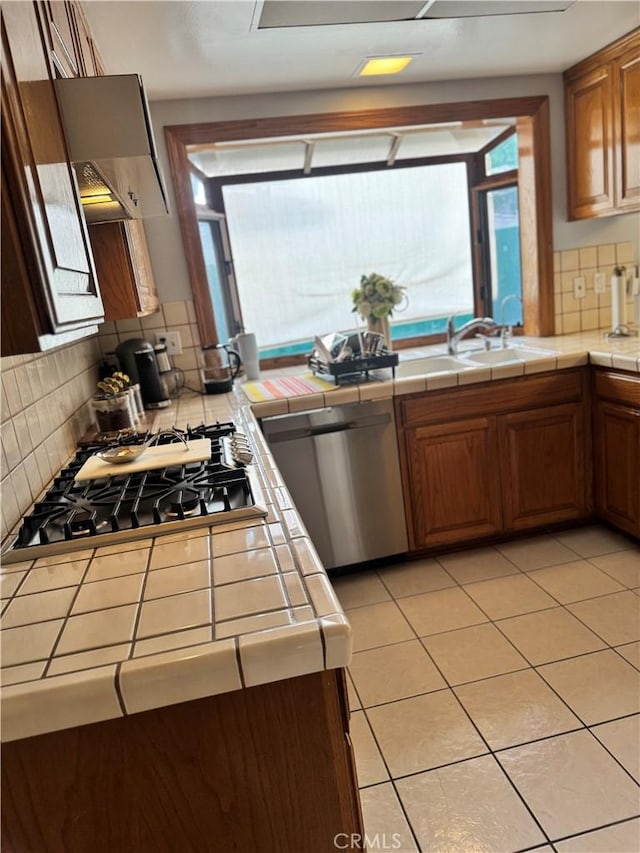 kitchen featuring tile countertops, stainless steel appliances, decorative backsplash, light tile patterned flooring, and a sink