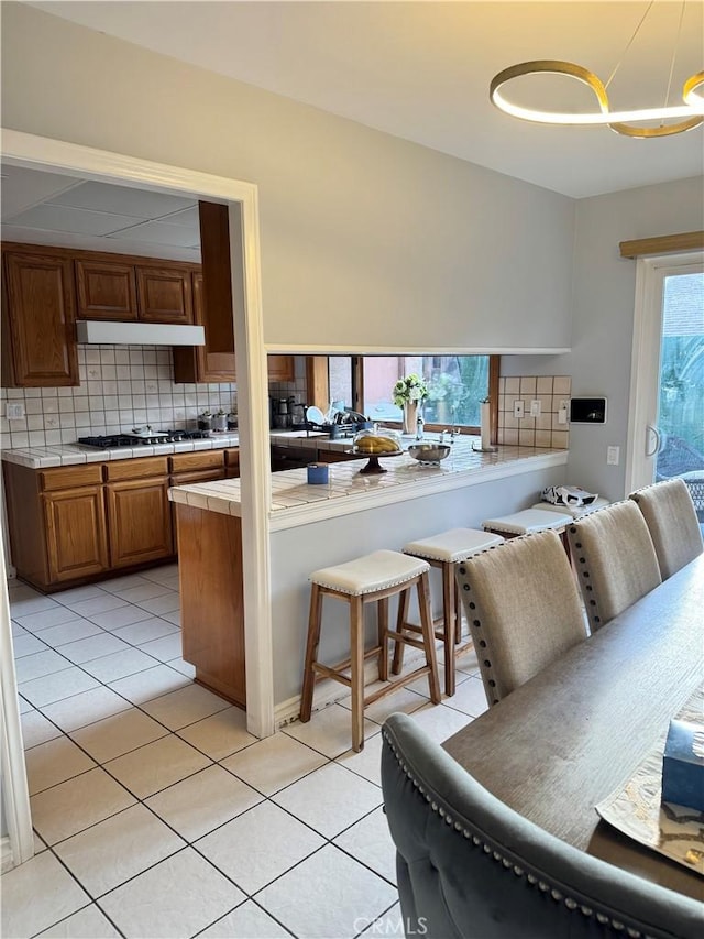 kitchen with cooktop, light tile patterned floors, decorative backsplash, tile countertops, and under cabinet range hood