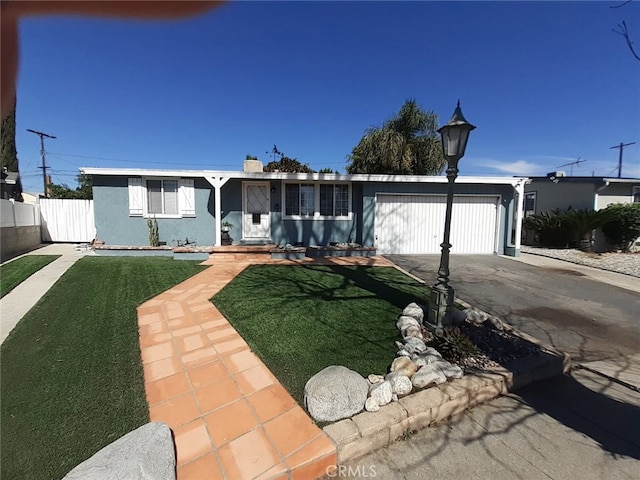 view of front of house featuring a front lawn, fence, stucco siding, a garage, and driveway