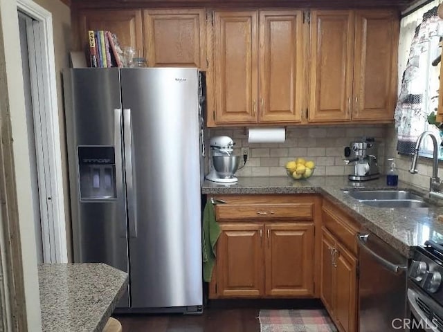 kitchen with appliances with stainless steel finishes, stone counters, a sink, and decorative backsplash