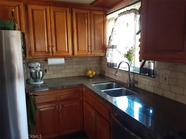 kitchen featuring brown cabinetry, a sink, backsplash, and fridge