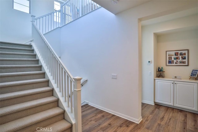 stairway featuring baseboards, a towering ceiling, and wood finished floors